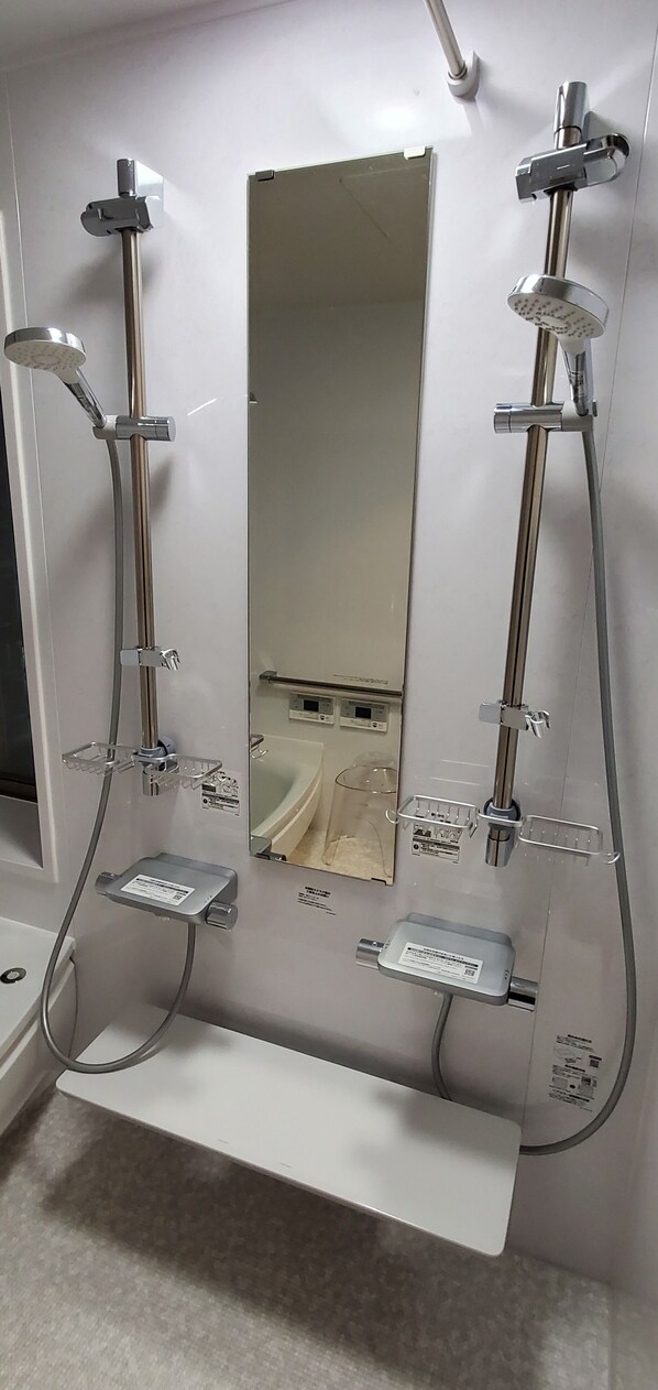 Un baño con dos cabezales de ducha, un espejo y un panel de control.