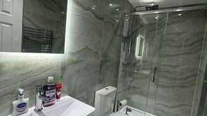 A modern bathroom with a marble wall, a glass shower enclosure, and a white vanity with toiletries. - Luxury Apartment in Knightsbridge (London)
