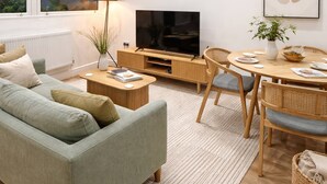 A modern living room with a sofa, TV, dining table, and chairs. - Luxury Apartment in Knightsbridge (London)