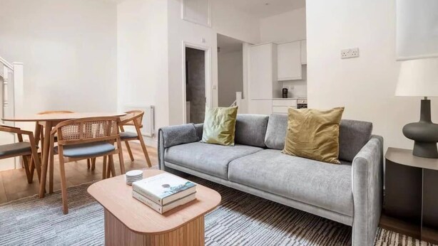 A modern living room with a grey sofa, wooden dining table, and a coffee table. - Luxury Apartment in Knightsbridge (London)
