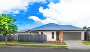 A single-story house with a garage, a fenced yard, and a tree. - The Entire House: Everything Is Within Easy Reach — Plus Theme Parks! (Coomera)