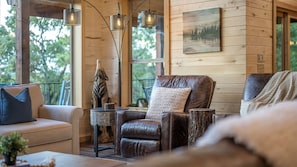 A cozy cabin interior with a leather couch, a wooden table, and a painting on the wall. - Luxury Ridge Top Cabin w/ Hot Tub & Epic Views (Broken Bow)