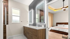 Ein modernes Badezimmer mit einem Holzkosmetikschrank, einem großen Spiegel und einem separaten Schlafzimmer mit Bett und Deckenventilator.