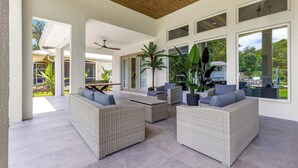 Ein großzügiger Patio-Bereich mit Korbmöbeln, großen Fenstern und einem Deckenventilator.