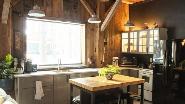 Una cocina con vigas de madera, un ventanal grande, una isla de madera y electrodomésticos modernos.