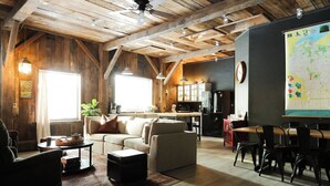 Un interior rústico con vigas de madera a la vista, un conjunto de sofás, una mesa de comedor con sillas, una zona de cocina y un mapa grande en la pared.