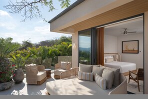 A modern bedroom with a large bed, a sofa, and a chair, with a view of greenery outside. - Villa Monarca in Punta Mita (Punta de Mita)