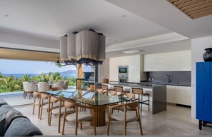 A modern kitchen with a glass island, a dining area with a glass table, and a view of the ocean. - Villa Monarca in Punta Mita (Punta de Mita)