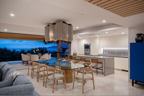A modern kitchen with a glass dining table, wooden chairs, and a view of the mountains. - Villa Monarca in Punta Mita (Punta de Mita)