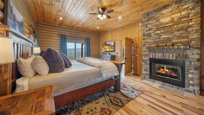 Ein Blockhaus-Interieur mit Bett, Kamin, Holzboden und Blick ins Freie.