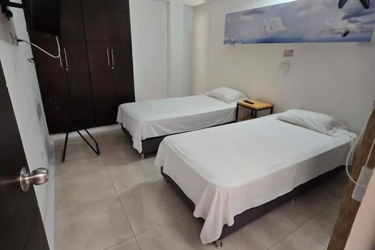 Une chambre avec deux lits simples, un ventilateur de plafond, une armoire et un téléviseur fixé au mur.
