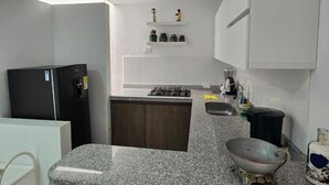 Cuina amb taulell de granat, nevera negra, fogó i armaris blancs.