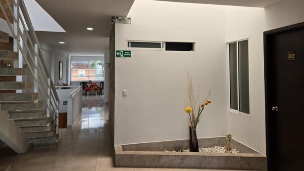 Rebedor d'hotel amb una escala, una recepció, un vas amb flors i una porta amb un número.