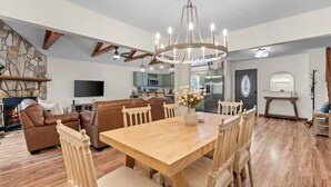A spacious living area with a wooden dining table, leather sofa, and a stone accent wall. - Owl & Ember - Walk to Coosawatee Resort Center! Grill, 2 Kings, 3 Smart TV's (Ellijay)
