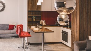 Eine moderne Küche mit einer Holzarbeitsplatte, ein Essbereich mit einem roten Stuhl und ein graues Sofa im Wohnzimmer.