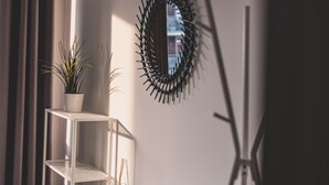 Ein Zimmer mit einem weißen Metallregal, das einen Topfpflanzen, einen an der Wand befestigten Spiegel und eine Stehlampe beherbergt.