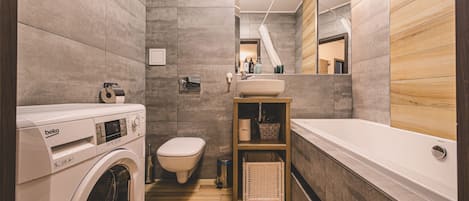 A modern bathroom with a washing machine, toilet, sink, and bathtub.