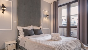 Ein modernes Hotelzimmer mit einem großen Bett, einem kleinen Nachttisch, einer Wandleuchte und Blick auf den Außenbalkon.