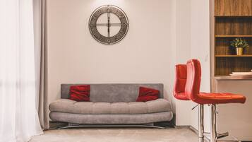A modern living room with a grey sofa, red cushions, a round wall clock, and a red bar stool.