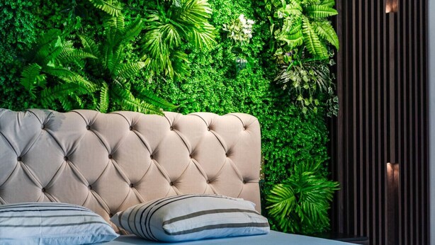 Une tête de lit capitonnée agrémentée d’oreillers, une couvre-lit à motifs et un mur d’un vert luxuriant.