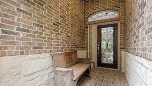 A narrow corridor with a bench, a door with a decorative metal grille, and a brick wall. - Family Retreat in Creekside • Relax & Unwind (Tomball)