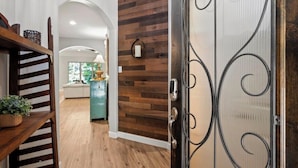 A hallway with a wooden floor, a metal door with a decorative handle, and a wall with a wooden panel design. - Family Retreat in Creekside • Relax & Unwind (Tomball)