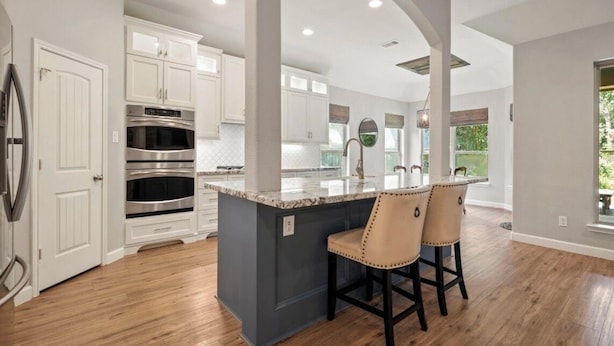 A modern kitchen with white cabinets, stainless steel appliances, a marble island, and a bar area with two chairs. - Family Retreat in Creekside • Relax & Unwind (Tomball)