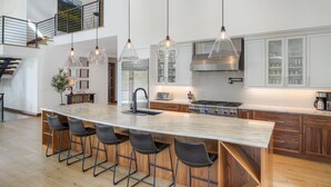 Een moderne keuken met een groot schiereiland, barkrukken, hanglampen en uitzicht op de omgeving.