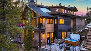 Een modern meerlaags huis met een jacuzzi, houten terras en grote ramen.