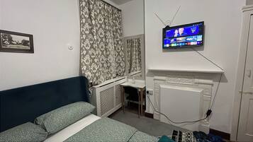 A bedroom with a bed, a television mounted on the wall, a radiator, and a small window.