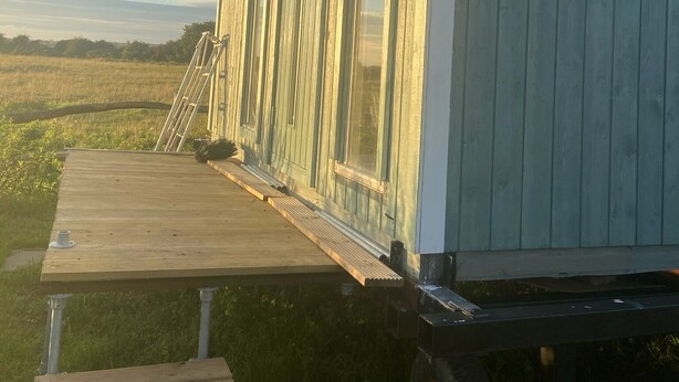 A wooden deck with a bench, a covered porch, and a view of a field.