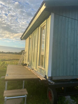 Una terraza de madera con un banco, un porche cubierto y vistas a un campo.