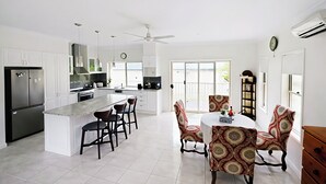 Una cucina moderna con isola centrale, sedie da pranzo, ventilatore a soffitto e un'ampia finestra.