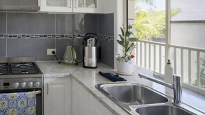 Cucina con piano cottura a gas, bollitore, macchina da caffè, lavello e finestra con vista sul verde.
