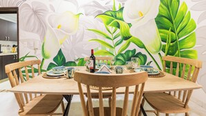 Un comedor con una mesa dispuesta para cuatro personas, rodeada de sillas, y un mural en la pared con flores y hojas.