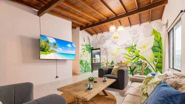Una sala de estar con televisor, una mesa de centro de madera, un sofá y un mural con flores tropicales.