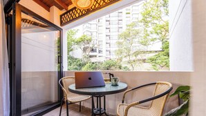 Un balcón con una computadora portátil, dos sillas de mimbre y vistas a un edificio y follaje.