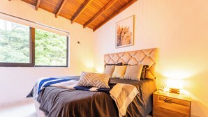 Un dormitorio con cama, mesita de noche, ventana y techo con vigas de madera.