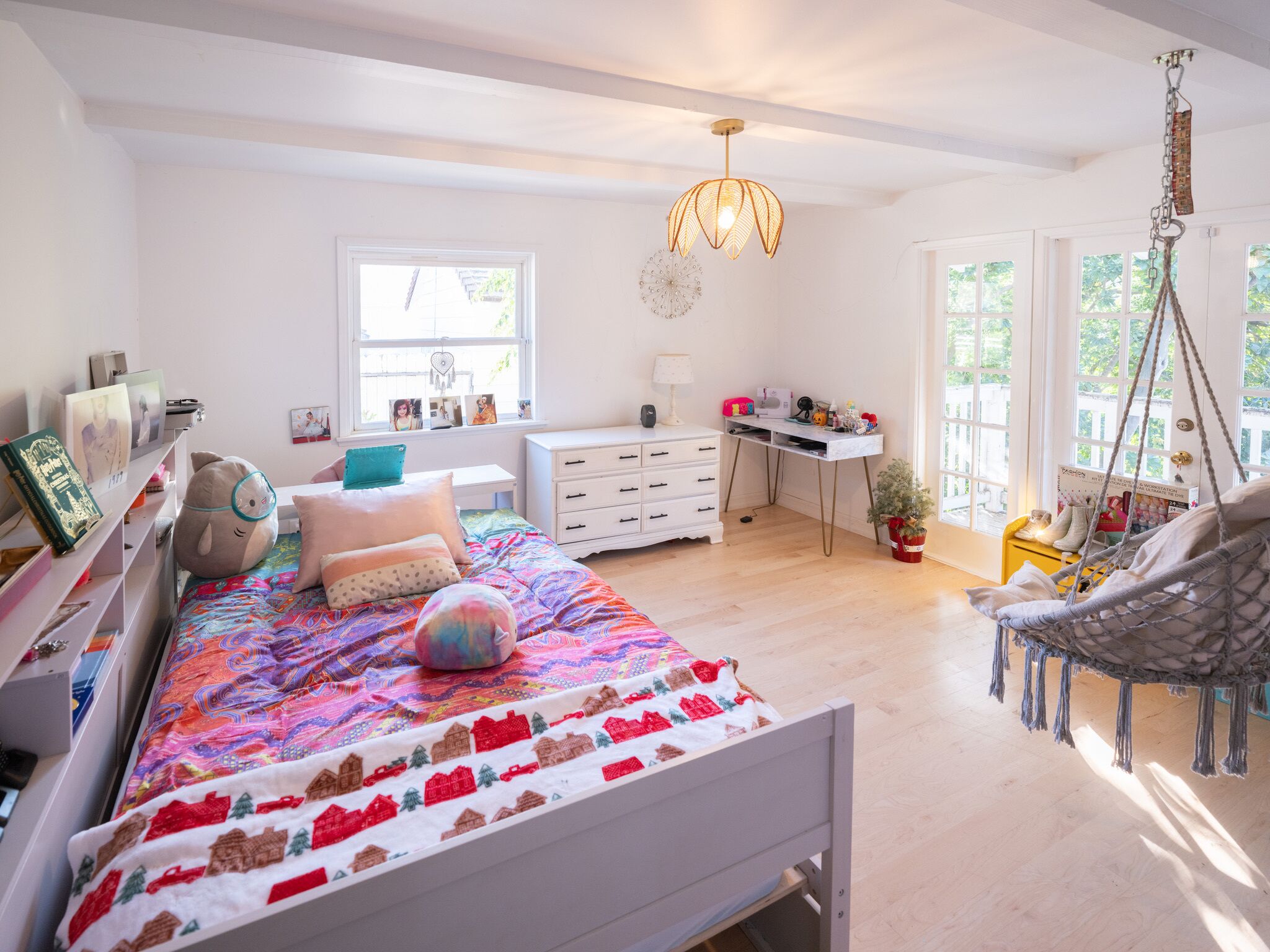 A bedroom with a bed, desk, chair, hanging swing, and a window with a view.