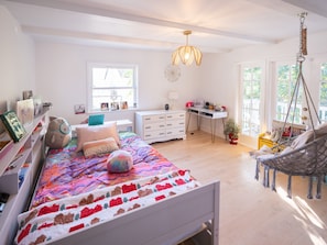 Une chambre avec un lit, un bureau, une chaise, une balançoire suspendue et une fenêtre donnant sur un beau paysage.