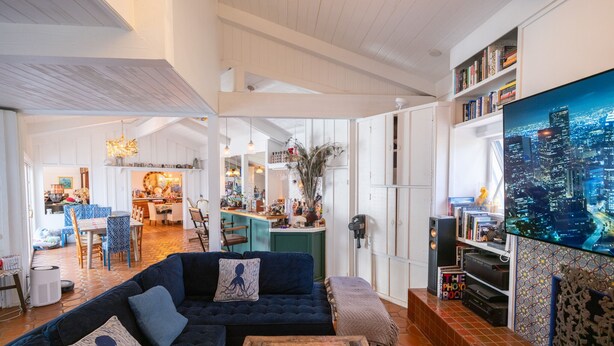 A spacious living area with a dark blue sofa, a wooden coffee table, and a cityscape TV. - Amazing 5-bedroom farmhouse in quaint Rolling Hills Estates with AC and nature! (Rolling Hills Estates)