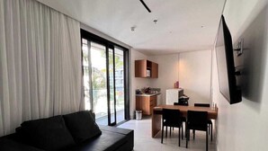 Un soggiorno moderno con un divano nero, un'area pranzo con tavolo e sedie, e un angolo cucina con pensili e un piano di lavoro.