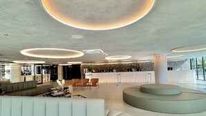 Una hall moderna con un'area salotto dalle linee curve, una reception e luci a soffitto circolari.