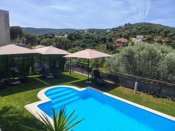 A swimming pool with a unique shape, surrounded by a well-maintained lawn, outdoor seating, and umbrellas.