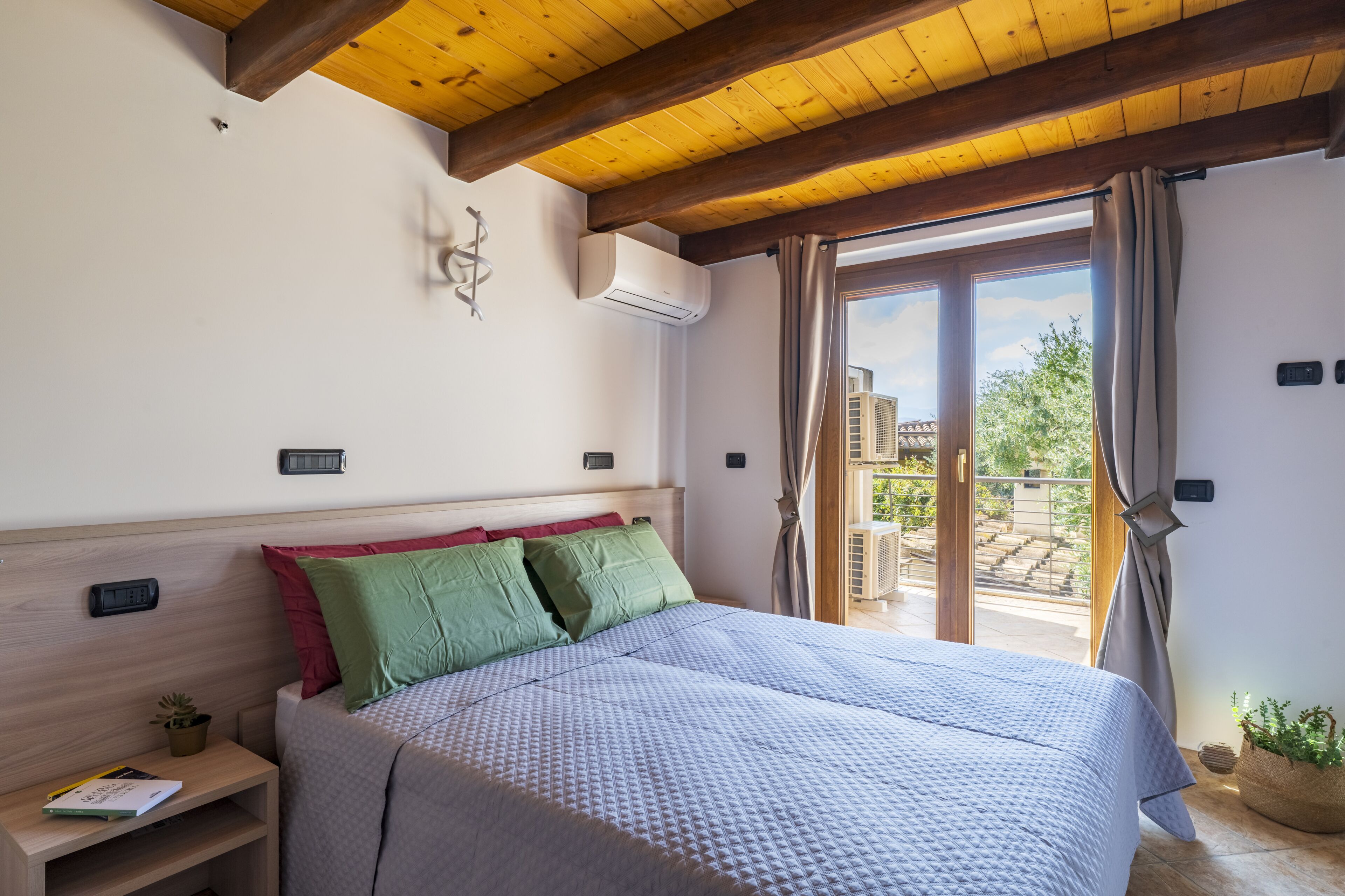 Een slaapkamer met een bed, nachtkastje, een wandairconditioner en uitzicht op buiten.