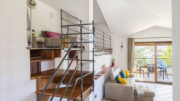 Een modern interieur met een houten trap, een bank met kleurrijke kussens en een balkon met tuinmeubilair.