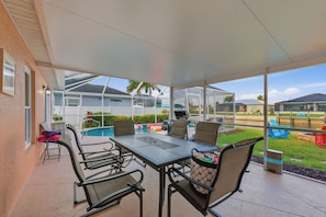A covered patio with a table and chairs, a pool, and a view of the surrounding area.