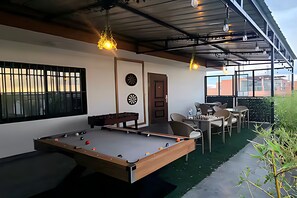 Een pooltafel met biljartballen, een dartbord en een deur naar een zithoek met tafels en stoelen.
