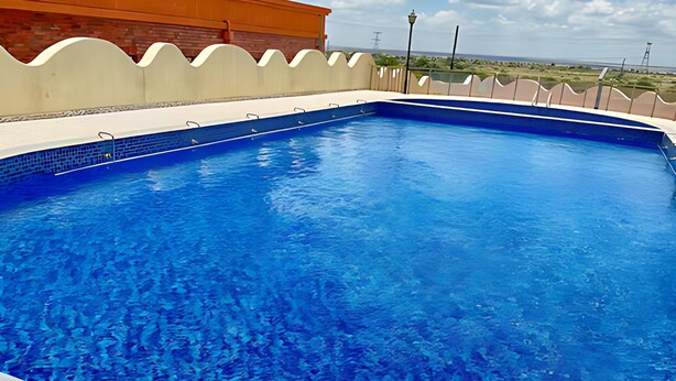 A swimming pool with a clear blue water surface, surrounded by a white tiled deck and a low white wall. - Luxury 6-Bed Penthouse with Sky Terrace (Nairobi)
