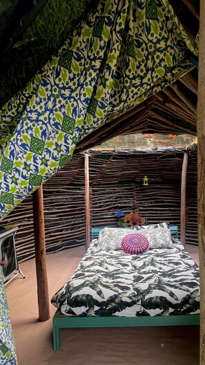 A room with a bed, a wooden bench, and a thatched roof.